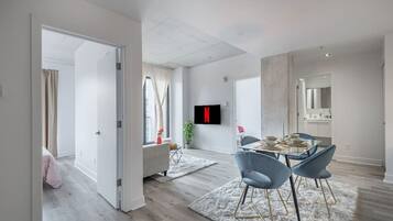 A modern interior with a dining area, a TV mounted on the wall, and a visible kitchen area.