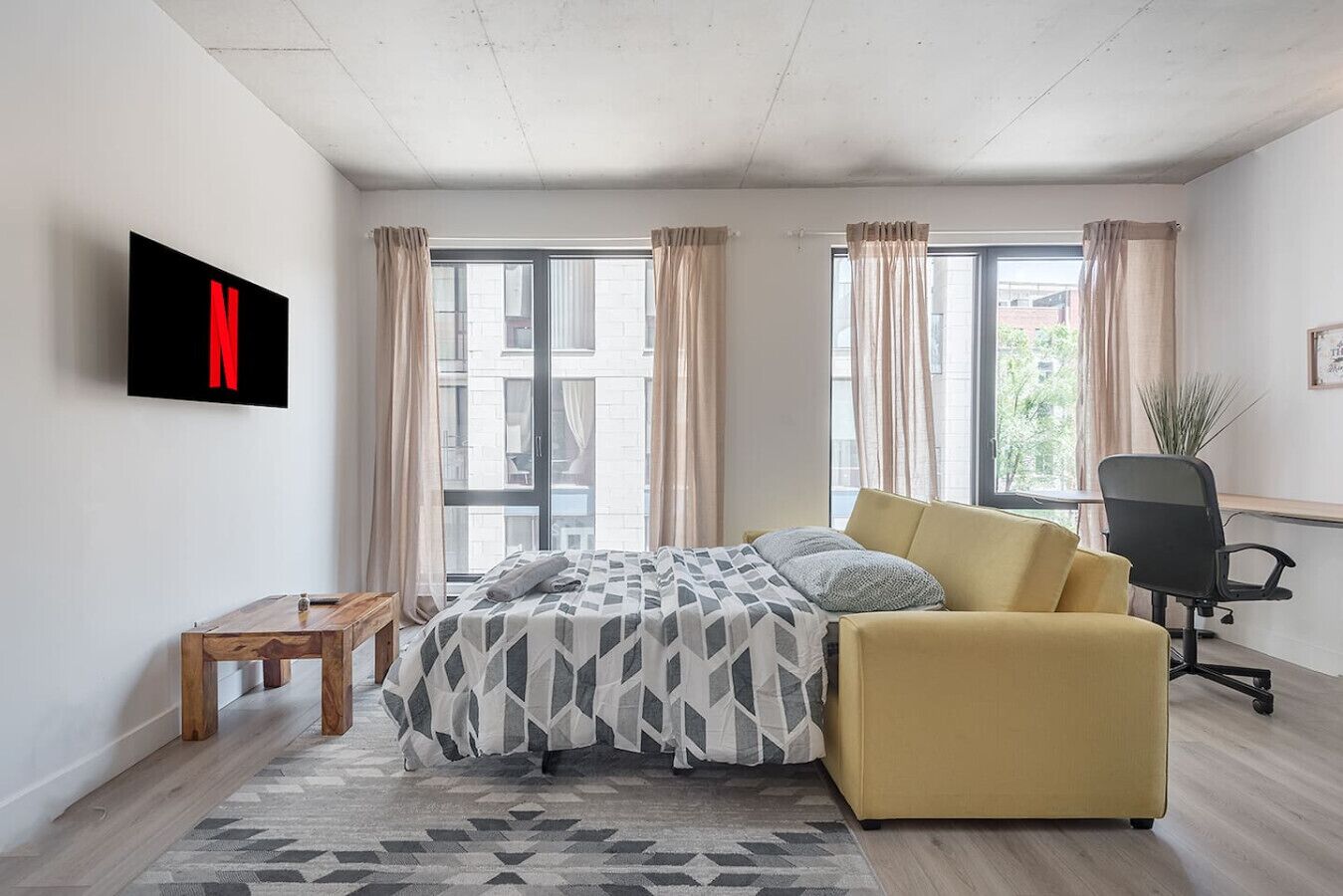 A modern bedroom with a bed, a sofa, a desk, and a TV mounted on the wall.