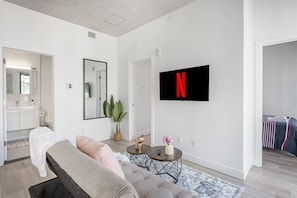 A modern living room with a sofa, a coffee table, a TV mounted on the wall, and a bathroom visible through an open door. - 2 Queen Beds- Panoramic View (Montreal)
