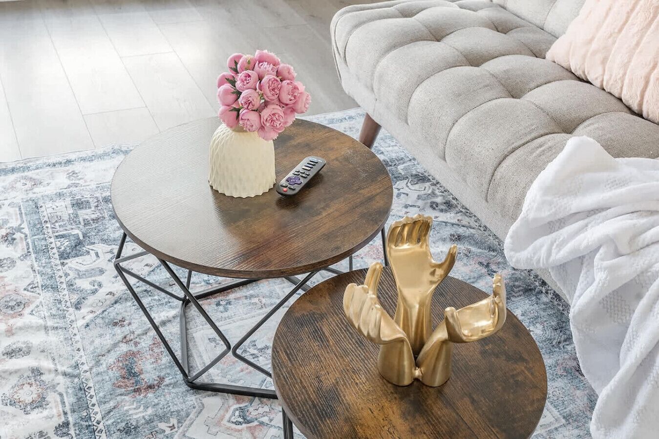 A round wooden coffee table with a vase of flowers and a remote control, a golden decorative object, and a patterned rug.