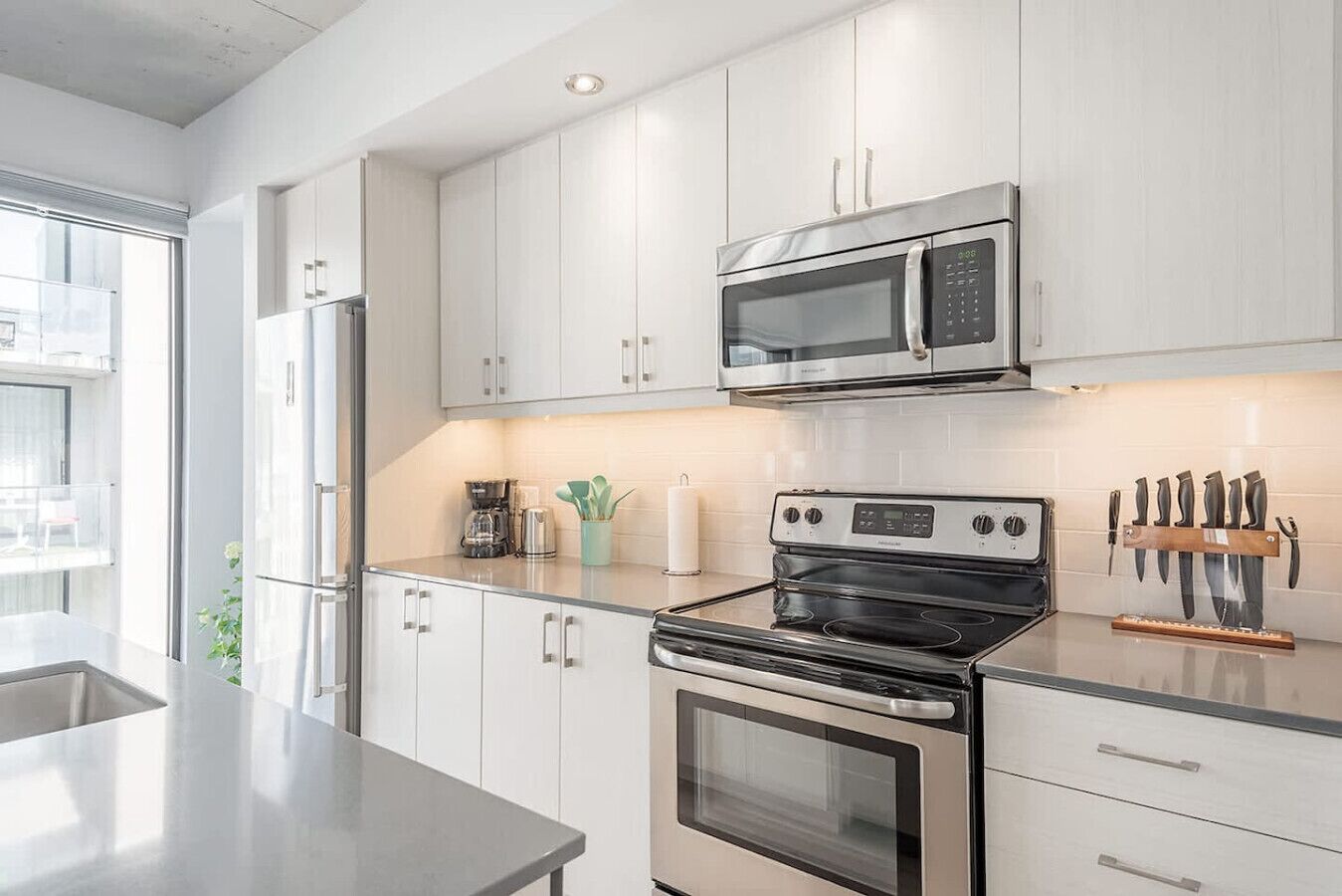 Una cocina moderna con electrodomésticos de acero inoxidable, armarios blancos y un organizador para cuchillos.