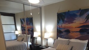 Una camera d'albergo con un letto grande, un comodino con una lampada, uno specchio e un quadro raffigurante un tramonto.