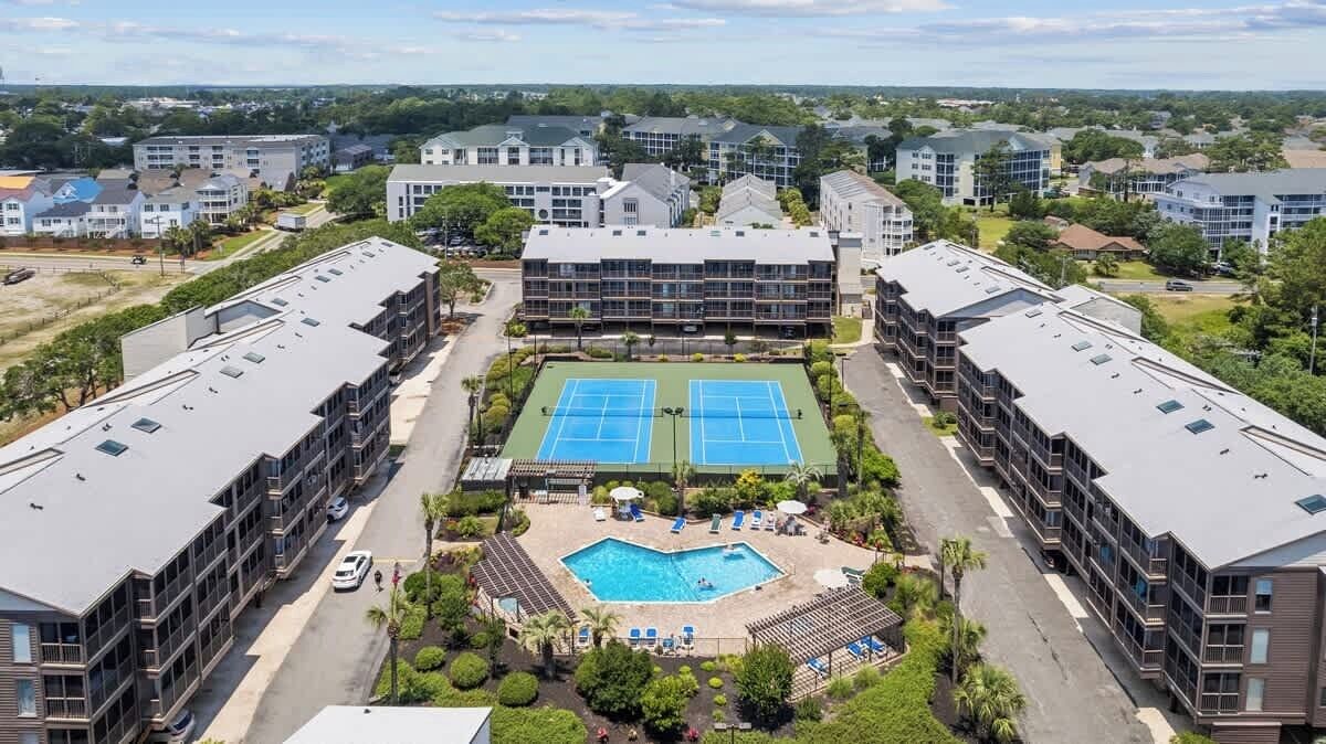 A residential complex with multiple apartment buildings, a tennis court, a swimming pool, and a landscaped courtyard.