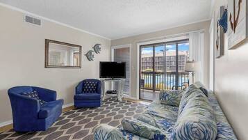 Una sala de estar con sofá, dos sillones, televisor y balcón con vistas.