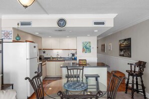 A kitchen with a central island, a refrigerator, and a dining area with chairs. - Ocean view Retreat 1BR Condo (Murrells Inlet)