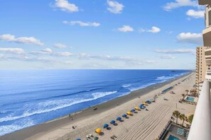 Blick auf einen Strand mit einer Reihe von Sonnenschirmen, einem Gebäude und blauem Himmel.