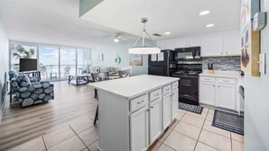 A modern kitchen with white cabinets, a black stove, and a dining area with a view. - The Tide Calls 1BR Ocean Front (Murrells Inlet)
