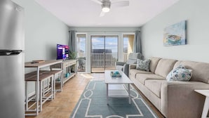 Een moderne woonkamer met een bank, salontafel en televisie. Er is een balkon met uitzicht.