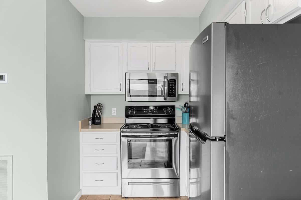 Una cocina con armarios blancos, un refrigerador de acero inoxidable, un microondas y un horno.