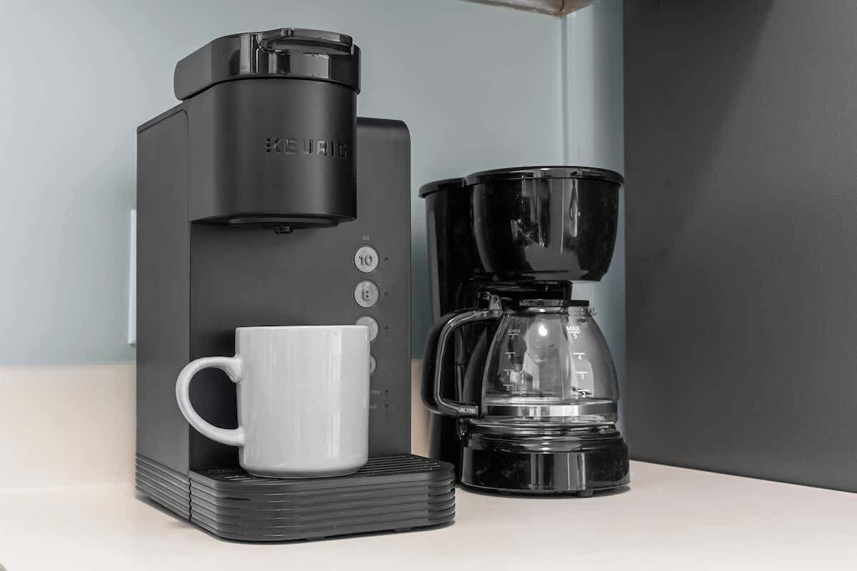 Una cafetera negra con una taza blanca sobre una encimera.