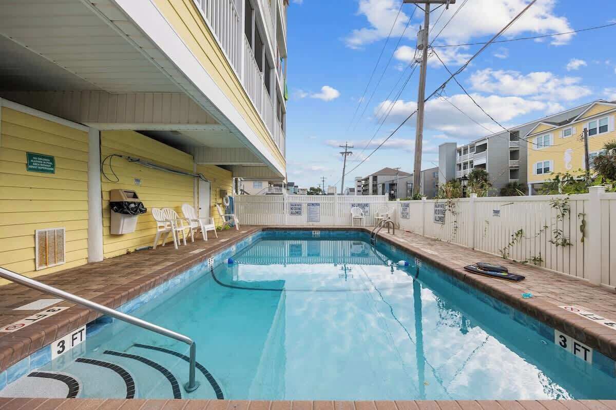 Une piscine dont la profondeur maximale est indiquée à 3 pieds, un espace abrité avec des chaises et une clôture blanche.