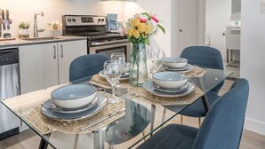 A modern kitchen with a dining table set for four, equipped with a microwave, stove, and coffee maker. - Square Vic | 2 Queens + Balcony Retreat (Montreal)