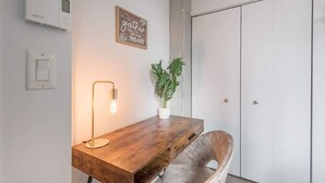 A room with a wooden desk, a modern floor lamp, a potted plant, a vintage chair, and a wardrobe. - Square Vic | 2 Queens + Balcony Retreat (Montreal)