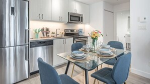 A modern kitchen with stainless steel appliances, a dining area with a glass table, and blue chairs. - Square Vic | 2 Queens + Balcony Retreat (Montreal)