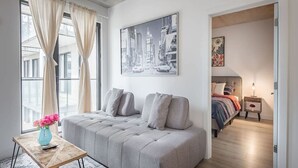 A modern living room with a sofa, a coffee table, a painting, and a view of the city. - Square Vic | 2 Queens + Balcony Retreat (Montreal)