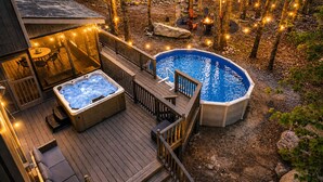 Eine Terrasse mit Whirlpool und Pool, umgeben von Bäumen und Lichterketten.
