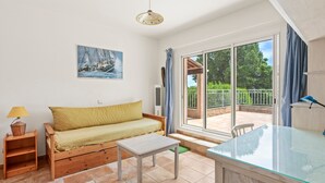 A room with a sofa, a small table, a glass-top table, a lamp, a painting, and a view through a sliding door. - La Maison de Valérie: Charming Provençal House Near the Beach for 6 Guests (La Croix-Valmer)