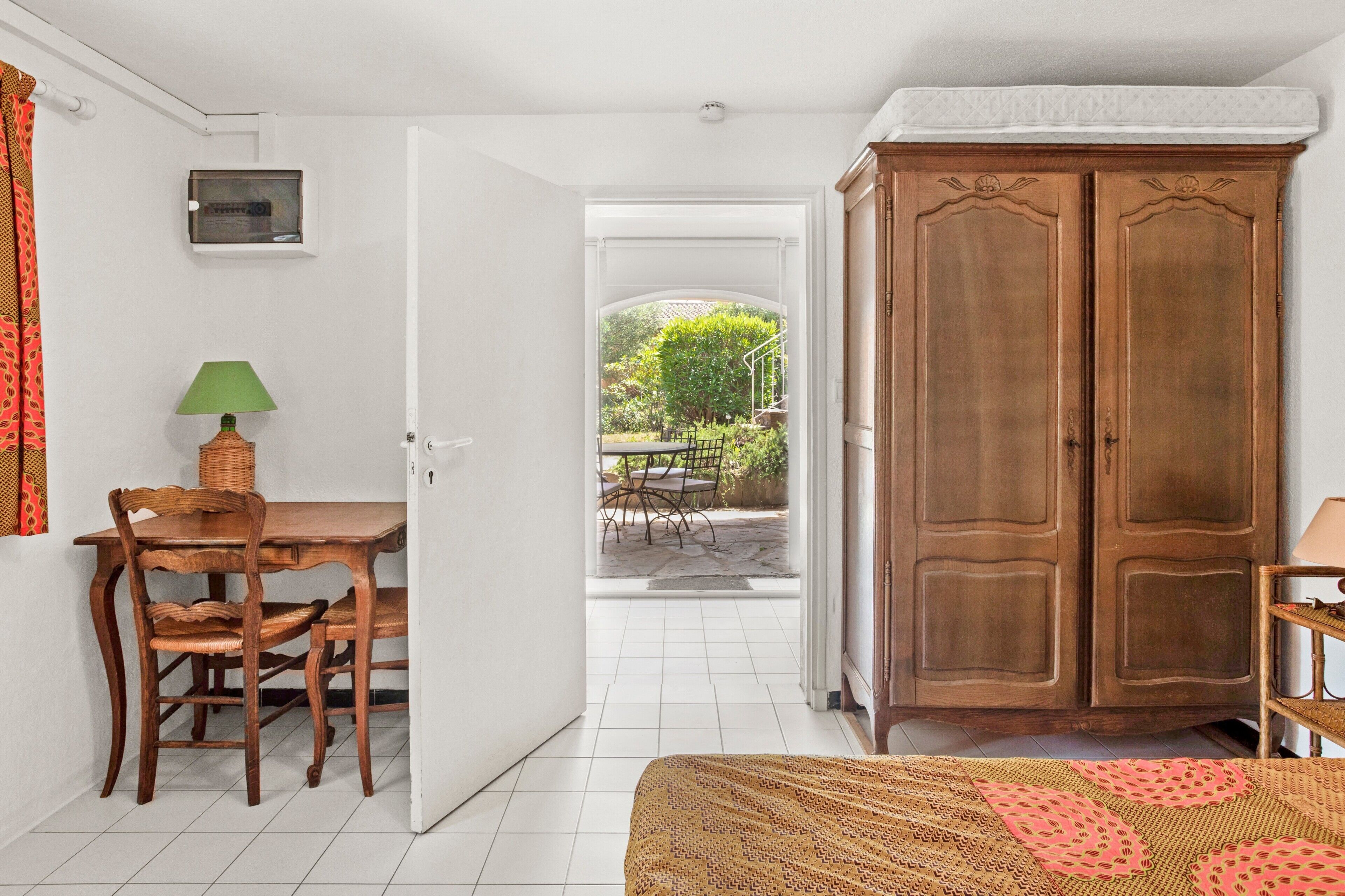 Ein Zimmer mit einem Bett, einem Holzschrank, einem Esstisch mit Stühlen und Blick auf einen Garten.