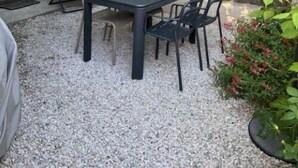 A stone building with a gravel patio, a table with chairs, and a tree providing shade. - Nine - PEYRIAC DE MER (PEYRIAC DE MER)
