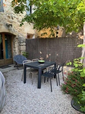 A stone building with a gravel patio, a table with chairs, and a tree providing shade. - Nine - PEYRIAC DE MER (PEYRIAC DE MER)