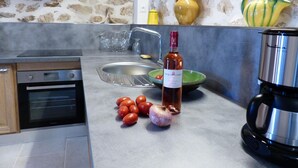 A kitchen with a stove, oven, sink, and various kitchen items like tomatoes, garlic, and a wine bottle. - Nine - PEYRIAC DE MER (PEYRIAC DE MER)