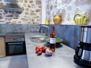 A kitchen with a stove, oven, sink, and various kitchen items like tomatoes, garlic, and a wine bottle. - Nine - PEYRIAC DE MER (PEYRIAC DE MER)