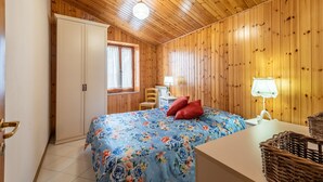 Et værelse med trævægge, en seng med blomstret sengetøj, et skrivebord med lampe og et garderobeskab.