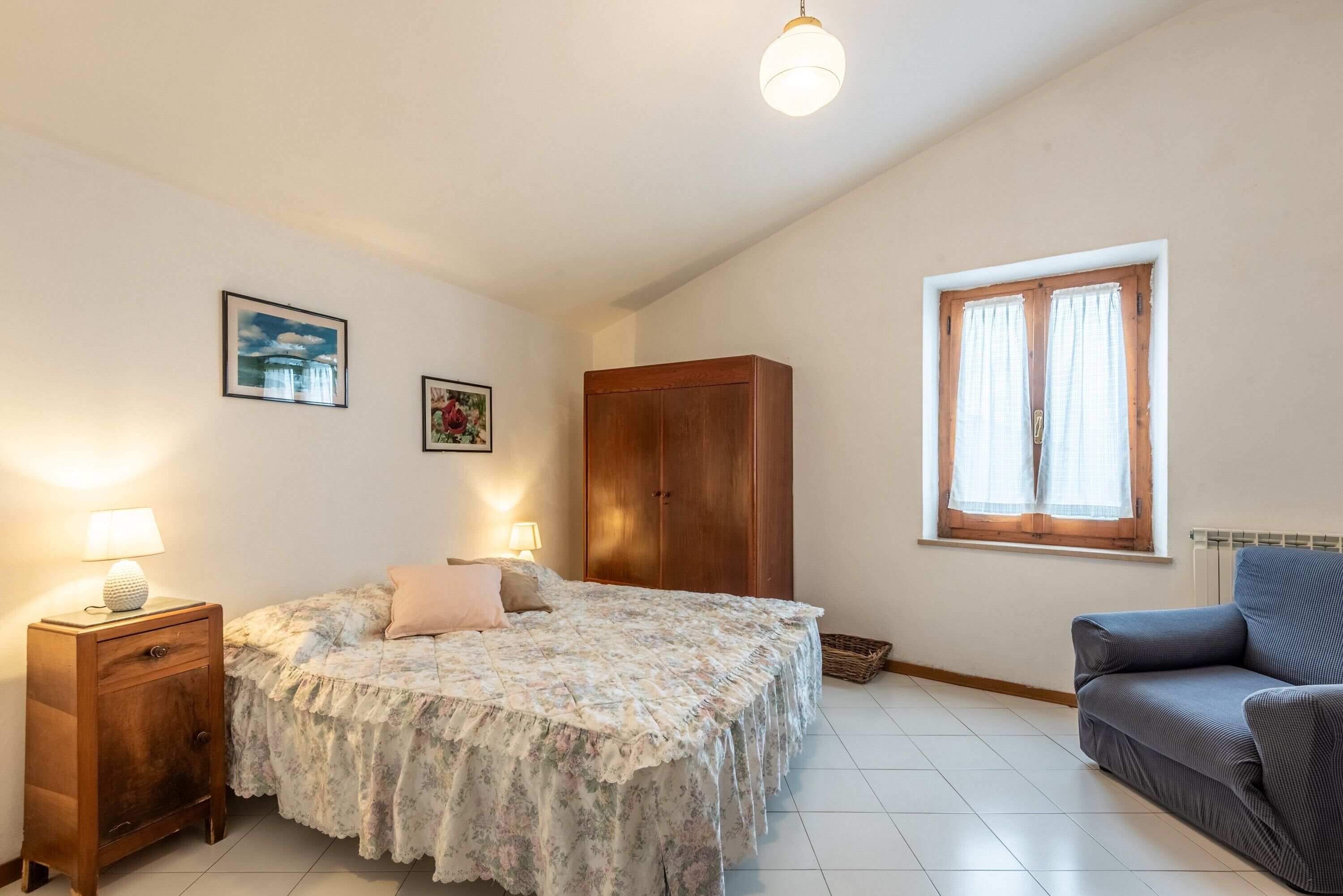 A bedroom with a bed, bedside tables, a wardrobe, a window with curtains, and a sofa.