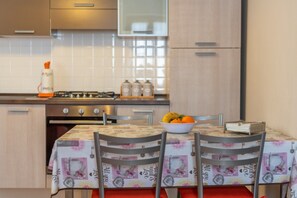 Une cuisine avec une table mise pour deux, une cuisinière à gaz et un saladier de fruits sur la table.