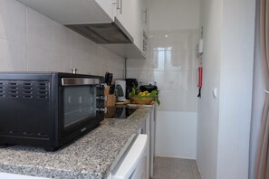 Una cocina con microondas, cafetera y frutero sobre la encimera.