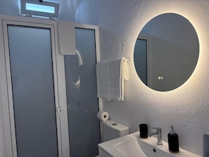 Un baño con un espejo redondo, un lavabo y un inodoro.