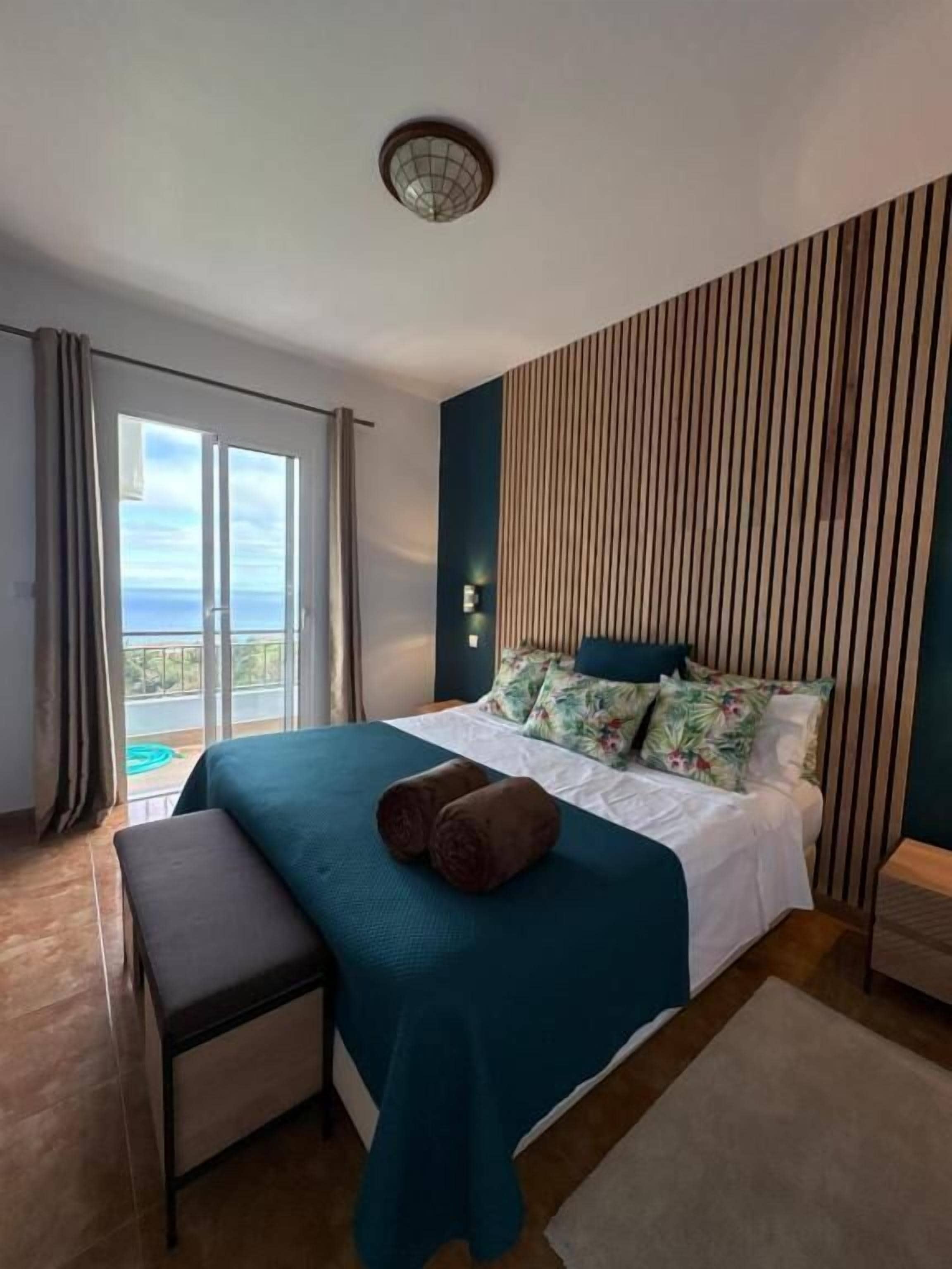 Une chambre d’hôtel moderne avec un grand lit, un banc, une vue sur l’extérieur et un luminaire au plafond.