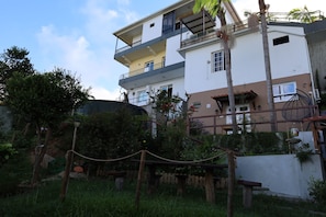 A multi-story residential building with balconies, a garden area with a rope barrier, and a street lamp. - Villa Alta Vista (Sao Jorge)