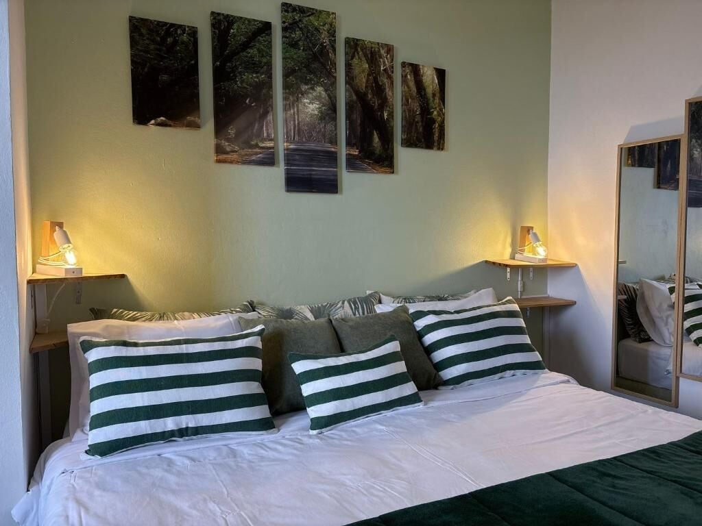 A hotel room with a bed, pillows, a nightstand, a lamp, and wall art.