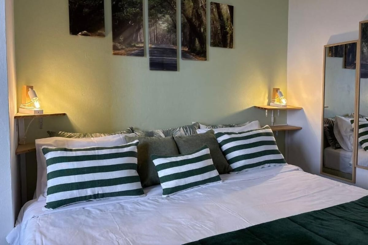 Una habitación de hotel con cama, almohadas, una mesita de noche, lámpara y decoración en la pared.