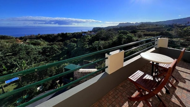A balcony with a table and chairs, overlooking a coastal landscape with hills and a clear sky. - Villa Alta Vista (Sao Jorge)