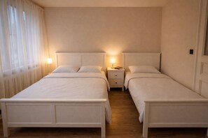 Une chambre double avec deux lits, une table de chevet avec une lampe et une fenêtre avec des rideaux légers.