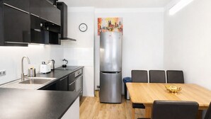 A compact kitchen with a sink, toaster, kettle, and a stainless steel refrigerator. There is a dining table with chairs and a painting on the wall. - Morning in Prague – Cozy Entire Home for 15, 1 min to Tram, 4 Rooms & 2 Kitchens (Praha2)