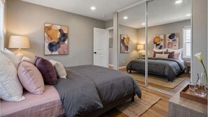 Ein Schlafzimmer mit einem großen Bett, einem Nachttisch, einem Spiegel und abstrakter Wandkunst.