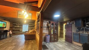 Un interior de cabaña acogedor con suelo de madera, un sofá, un televisor, un armario y una zona de cocina.