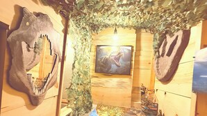 Una habitación con un mural con tema de dinosaurios, un cuadro en la pared y una pequeña figura en un estante.