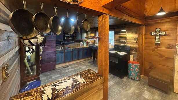 Una cocina rústica con ollas colgantes, un letrero de bienvenida, una cruz y un banco de madera.