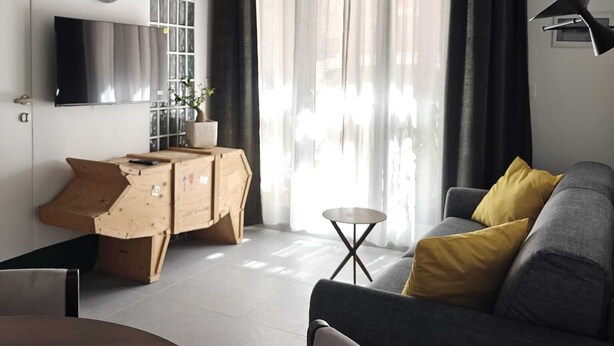 Ein modernes Wohnzimmer mit einer Couch, einem kleinen Tisch, einem Fernseher und einem Fenster mit Vorhängen.