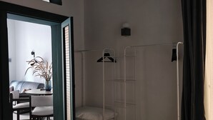 Ein Schlafzimmer mit einem Bett, einem Schreibtisch und einem Stuhl. Ein Fenster bietet Blick auf eine Pflanze und ein Sofa.