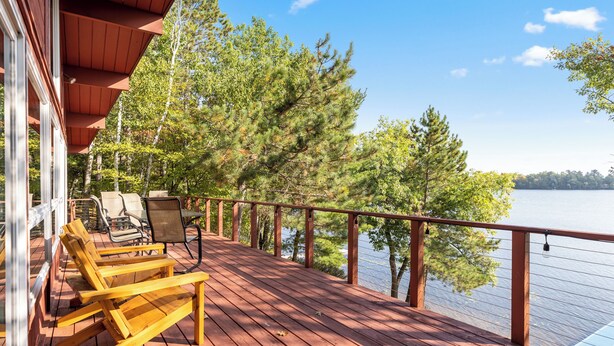 A wooden deck with outdoor furniture, overlooking a lake with trees. - The Lakeside Lookout - Lakefront 4BR Cabin - Dock, Kayaks, Swim Raft + Game Shed (Cushing)