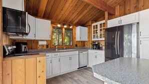A kitchen with wooden cabinets, a stainless steel refrigerator, and a granite countertop. - The Lakeside Lookout - Lakefront 4BR Cabin - Dock, Kayaks, Swim Raft + Game Shed (Cushing)