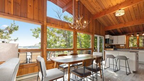 A wooden interior with a dining table, chairs, a kitchen area, and large windows. - The Lakeside Lookout - Lakefront 4BR Cabin - Dock, Kayaks, Swim Raft + Game Shed (Cushing)
