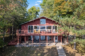 A red cabin with a balcony, large windows, and a deck with outdoor furniture.
