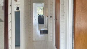 A hallway with white siding walls, a wooden door frame, and a grey couch in the background. - 3 bedroom lovely home in Sjællands Odde (Sjællands Odde)