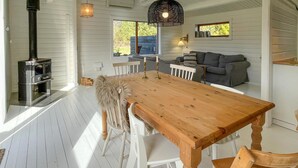 A wooden dining table with chairs, a sofa, a fireplace, and a window with a view of greenery. - 3 bedroom lovely home in Sjællands Odde (Sjællands Odde)
